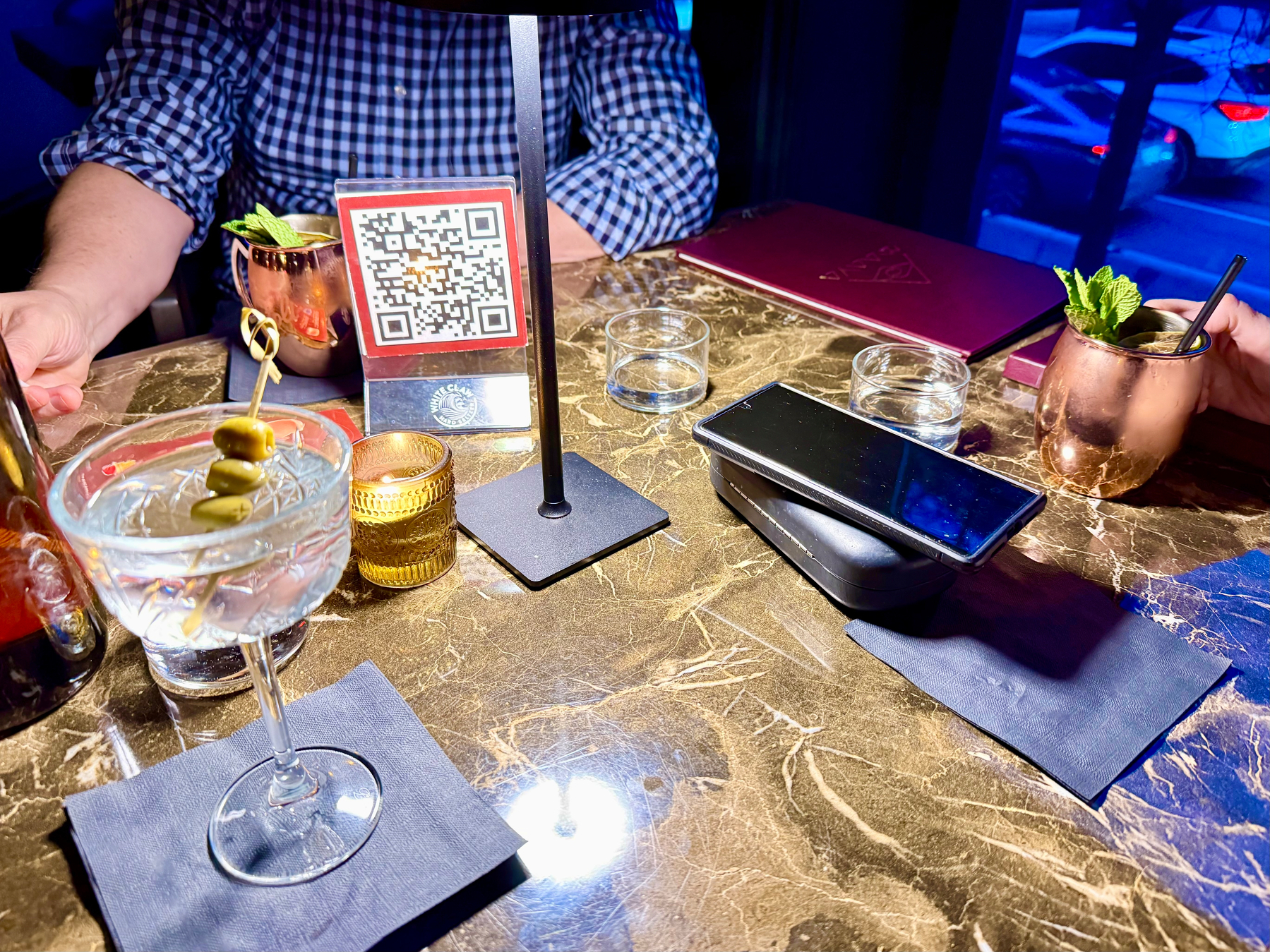 Two people are sitting at a table with cocktails and candles on a marble surface.