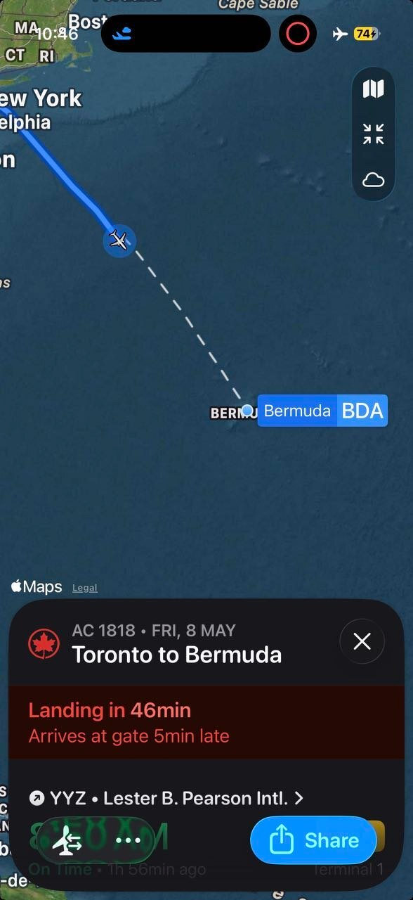 A flight tracking map shows an Air Canada flight AC 1818 from Toronto to Bermuda over the Atlantic Ocean. The flight path is displayed as a dashed line, with a solid blue line marking the completed portion of the journey from the northeastern United States toward Bermuda. The airplane icon is currently positioned over the ocean, southeast of New York and Philadelphia, heading toward Bermuda. Bermuda is marked with a blue label and the airport code BDA. At the bottom of the image, a flight status panel indicates the flight is landing in 46 minutes and will arrive 5 minutes late, departing from Toronto Pearson International Airport. The Apple Maps interface is visible, including a small map control panel on the right side.