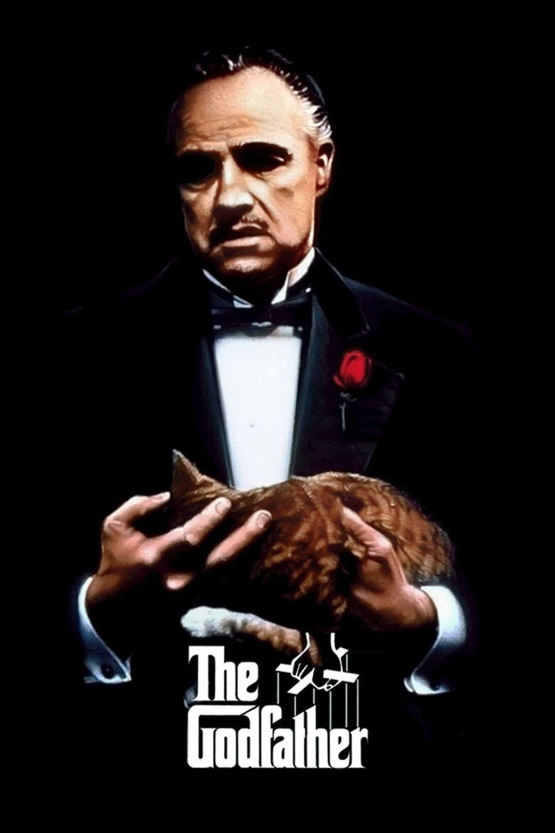 A man in a black tuxedo with a white dress shirt and black bow tie is holding a brown tabby cat in his hands. A single red rose is pinned to his lapel. His expression is stern and serious, and he is set against a completely black background. Below the cat is a white logo with the words "The Godfather," featuring a marionette hand holding puppet strings as part of the design.