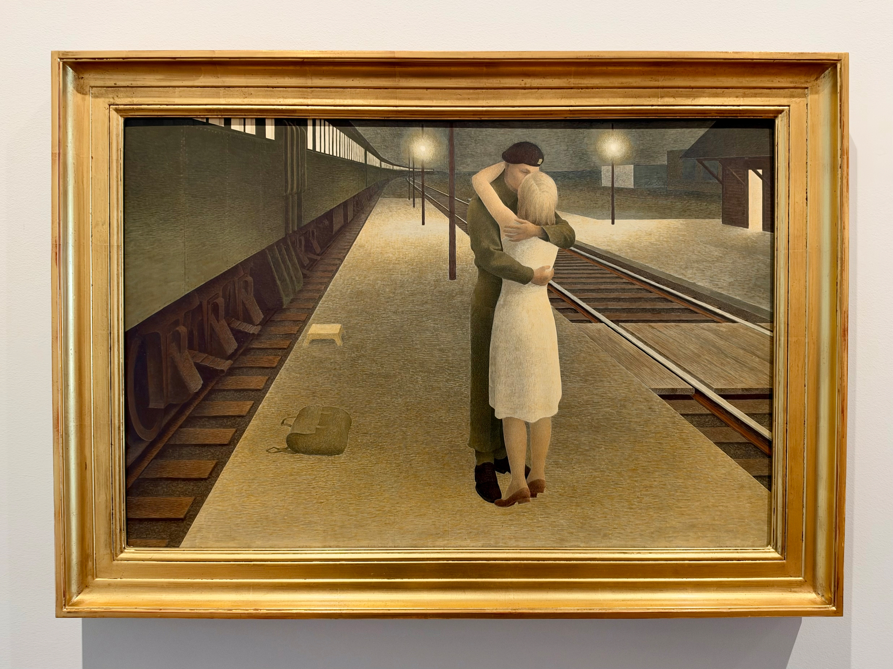 A couple embraces on an empty train platform at night, surrounded by muted tones and dim lighting.