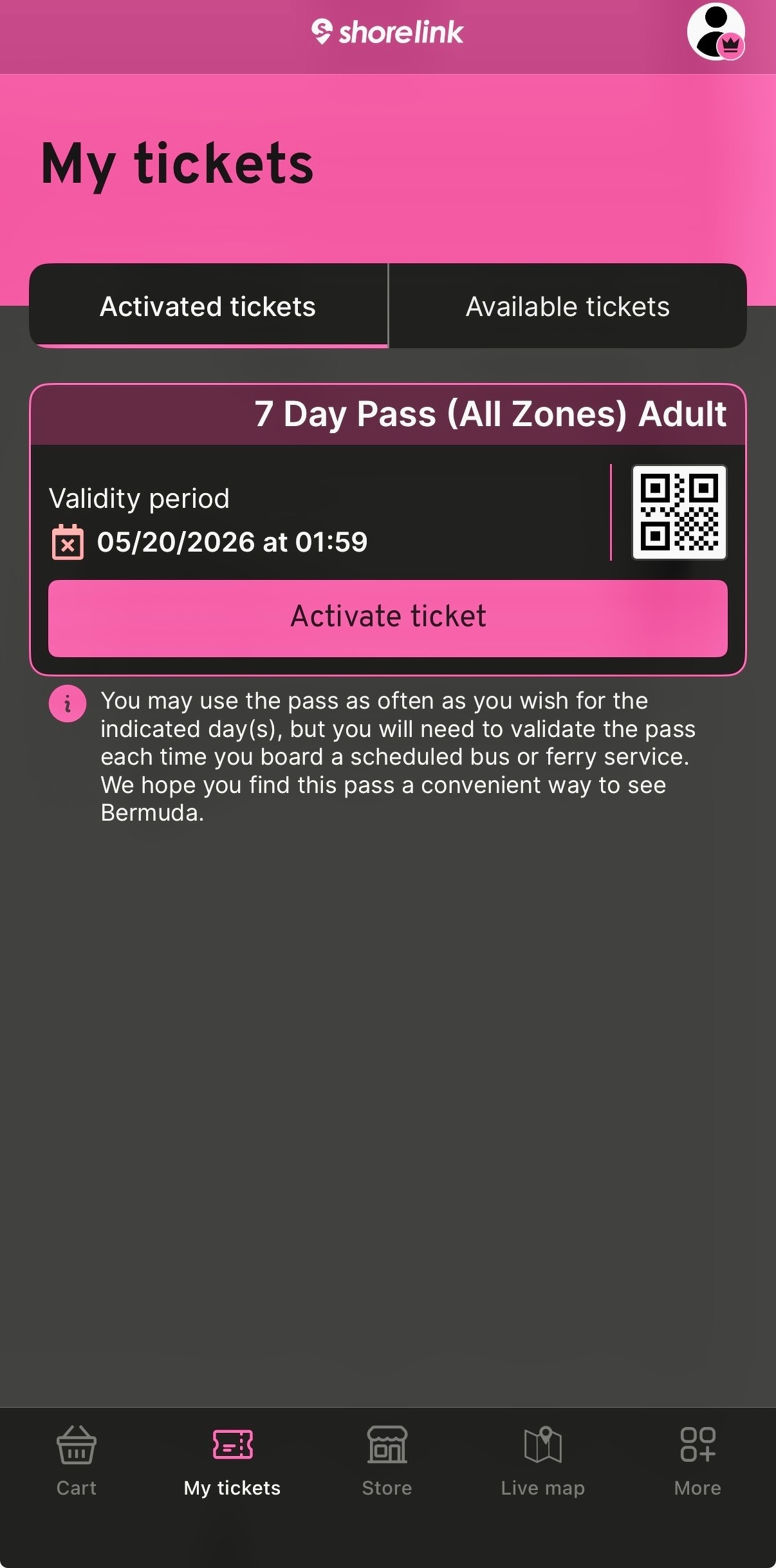 A smartphone screen showing the Shorelink app open to the “My tickets” section. The top of the screen has a pink header with the Shorelink logo and a profile icon on the right. Below, there are two tabs: “Activated tickets” (highlighted) and “Available tickets.” A ticket is displayed for a “7 Day Pass (All Zones) Adult” with a validity period listed as “05/20/2026 at 01:59.” To the right of this is a small QR code. A large pink button labeled “Activate ticket” is below the ticket details. A note beneath reads: “You may use the pass as often as you wish for the indicated day(s), but you will need to validate the pass each time you board a scheduled bus or ferry service. We hope you find this pass a convenient way to see Bermuda.” At the bottom, a black navigation bar has icons for Cart, My tickets (highlighted in pink), Store, Live map, and More. The background is a dark grey.
