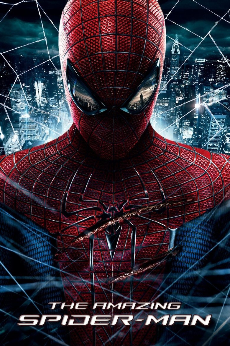A close-up image of Spider-Man in his red and blue suit, with the red sections covered in a honeycomb-like texture and black webbing patterns. His large, reflective eye lenses show a faint reflection of the city skyline. Behind him is a nighttime cityscape filled with illuminated skyscrapers, including the Chrysler Building, under a dark, cloudy sky. White spider webs are stretched across the image, framing Spider-Man. At the bottom, in bold metallic letters, the words read “THE AMAZING SPIDER-MAN.”