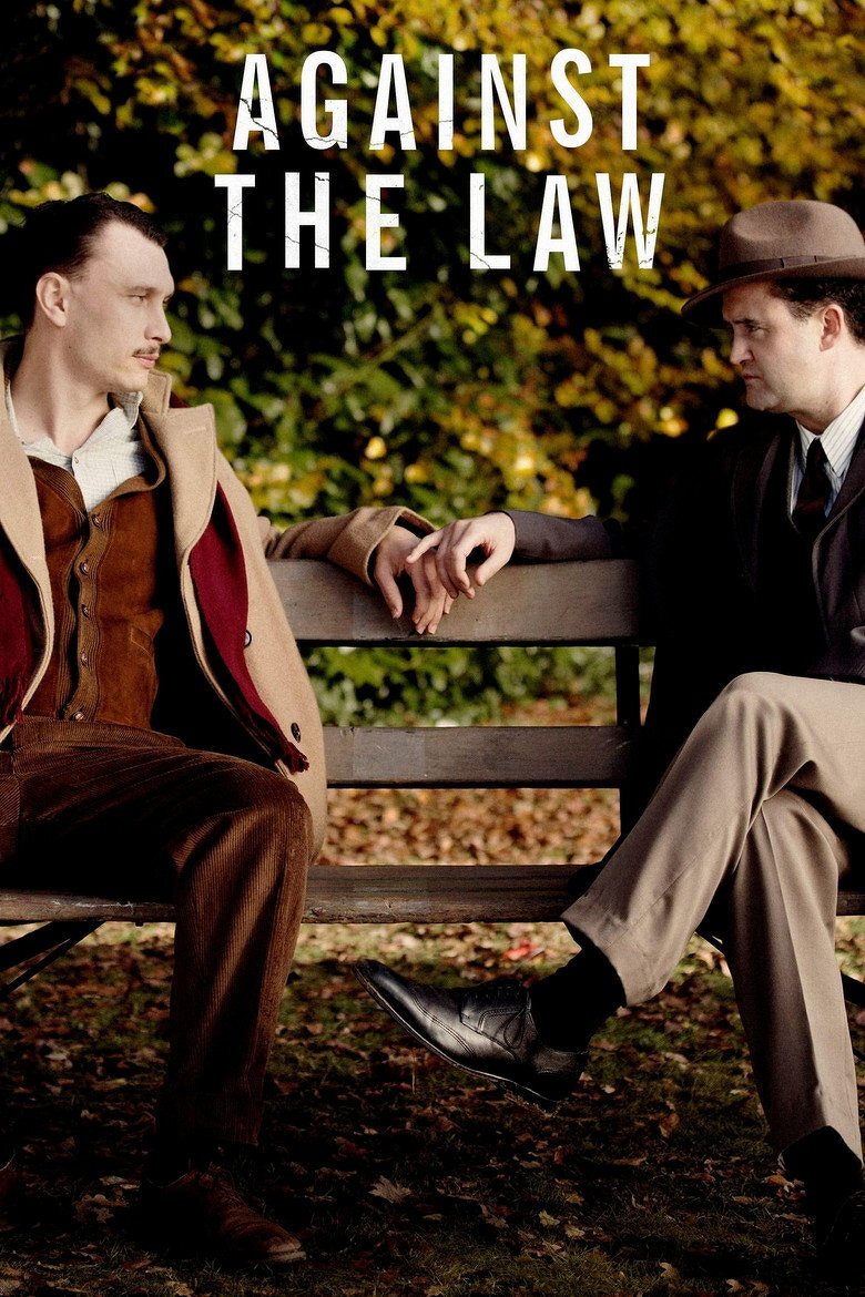 Two men are sitting on a wooden park bench surrounded by autumn leaves, with a backdrop of trees showing yellow and green foliage. The man on the left has short hair, a light moustache, and is wearing a tan coat with a red lining over a brown vest, a light collared shirt, and brown corduroy pants. He is leaning back slightly, resting his arm along the back of the bench. The man on the right is wearing a dark coat, a white shirt with a tie, tan pants, black socks, and black dress shoes, along with a brown fedora hat. He sits with his legs crossed, leaning towards the other man, and they are almost touching hands on the back of the bench. Above them, large white letters read “AGAINST THE LAW.”