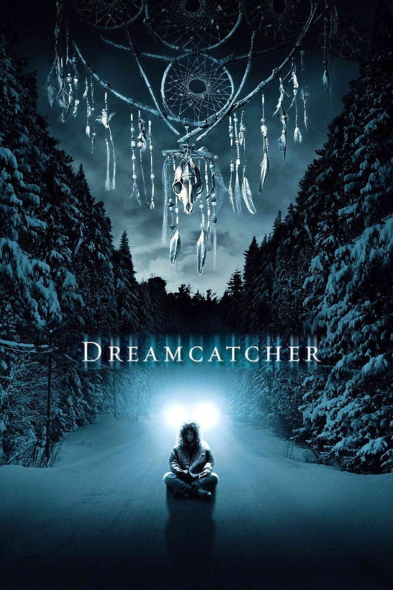 A snowy forest road at night is illuminated by the headlights of a vehicle in the distance. A person wearing a hooded winter coat sits cross-legged on the snowy road in front of the vehicle, their figure casting a shadow behind them. Above the scene, a large, eerie dreamcatcher hangs in the sky, adorned with feathers, beads, and a small animal skull in the centre. The sky is dark and filled with an ominous glow. The word "DREAMCATCHER" appears across the centre of the image in glowing, icy white letters.