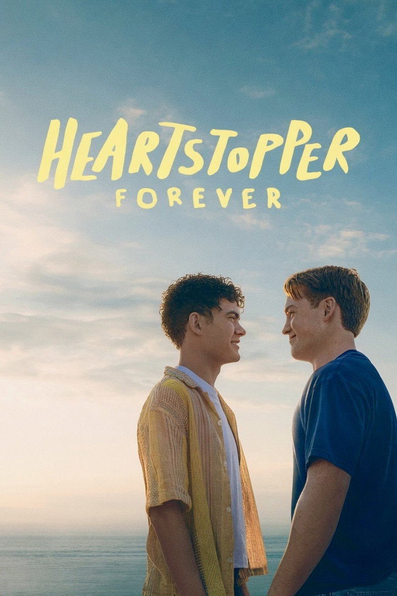 Two young men stand facing each other and smiling against a scenic backdrop of the ocean and a sky with soft clouds at sunset or sunrise. One wears a sheer yellow short-sleeve shirt over a white t-shirt, and the other wears a blue t-shirt. Above them, in large, hand-painted yellow letters, is the text “HEARTSTOPPER FOREVER.”