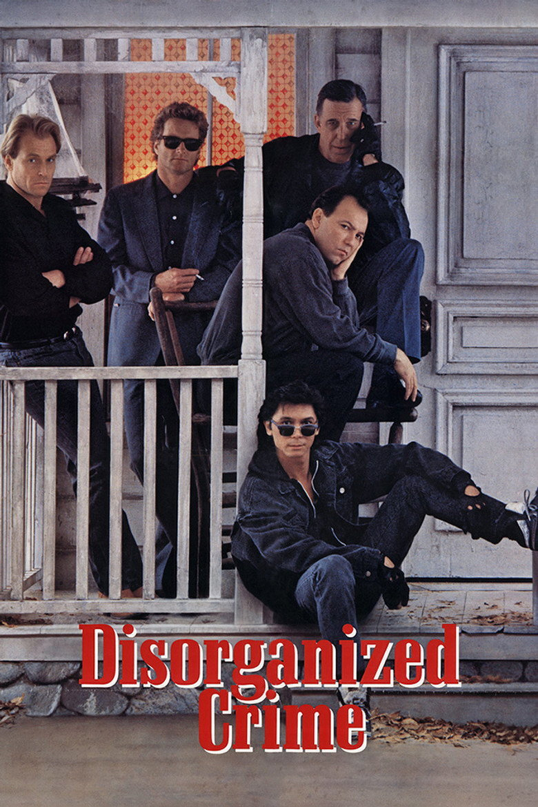 A group of five men poses on the porch of a weathered, white wooden house. One man leans against the porch railing with his arms crossed, wearing a black shirt and jeans. Another man in a grey suit and black sunglasses stands beside him, resting his hands on the top of a chair. Behind them, a man in dark clothing crouches on the porch with one hand on his face, while another man in a dark sweatshirt and pants sits with his chin resting on his hand, looking tired or contemplative. At the front, a man dressed in all black with a denim jacket and ripped jeans sits casually on the porch steps, wearing dark sunglasses and leaning back with one arm on his knee. The words “Disorganized Crime” appear at the bottom in large, bold, red and white letters. Dry leaves are scattered on the ground in front of the porch.