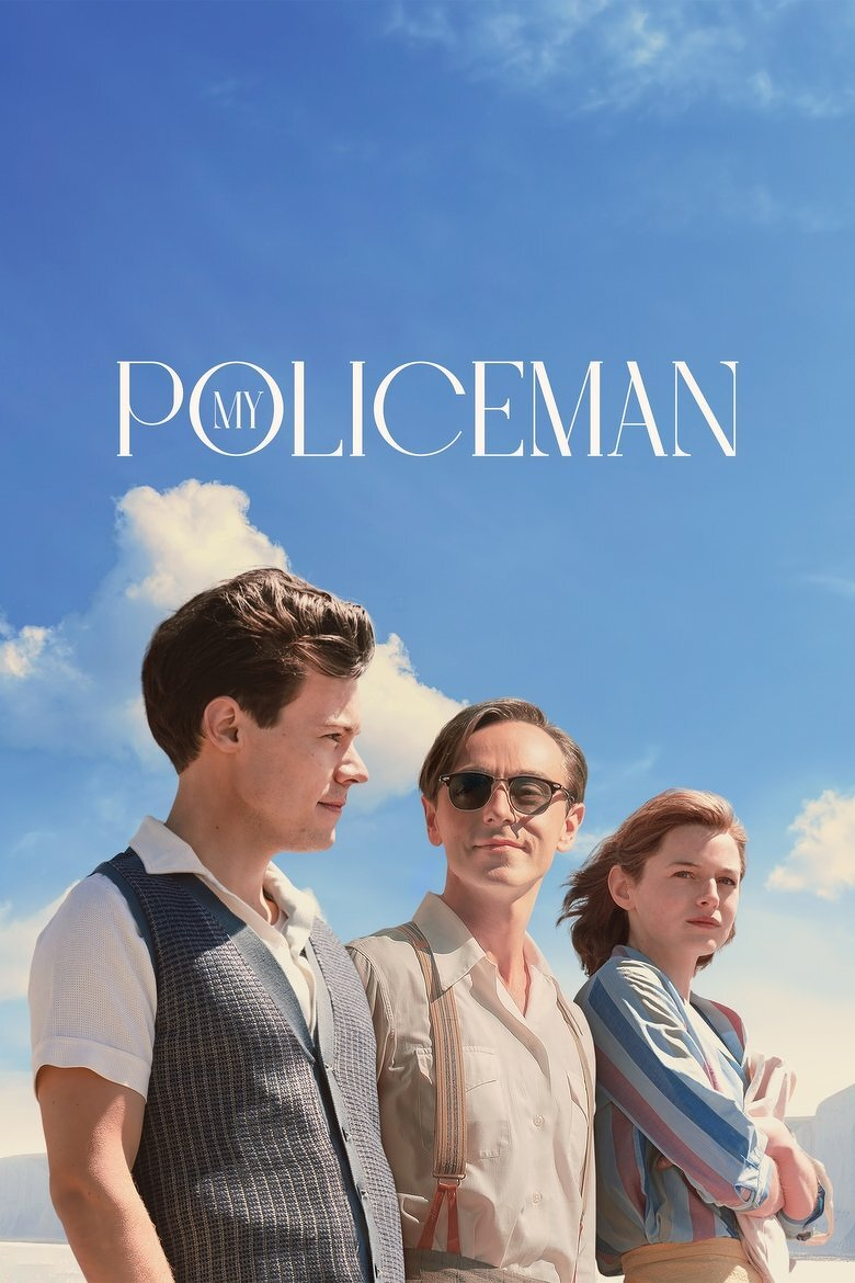 A movie poster featuring three people standing together under a bright blue sky with scattered clouds. On the left, a young man with short dark hair wears a white collared shirt under a patterned vest and looks to the right. In the centre, a man with light brown hair combed back wears sunglasses, a beige button-up shirt, and suspenders, gazing slightly upward. On the right, a woman with short reddish-brown hair wears a striped blue and pink blouse and light beige skirt, holding her arms close to her chest while looking ahead. The text at the top reads "MY POLICEMAN" in elegant white font, with the word "MY" set inside the "O" of "POLICEMAN." White cliffs and a calm, pale landscape are partially visible in the background.