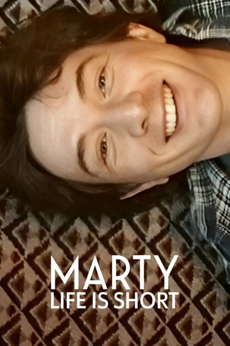 A young person with short dark brown hair is lying sideways on a patterned carpet, smiling broadly and looking relaxed. They are wearing a dark plaid shirt. The carpet has a diamond-shaped geometric pattern in shades of brown and beige. Superimposed text near the bottom of the image reads: “MARTY LIFE IS SHORT” in bold white capital letters.