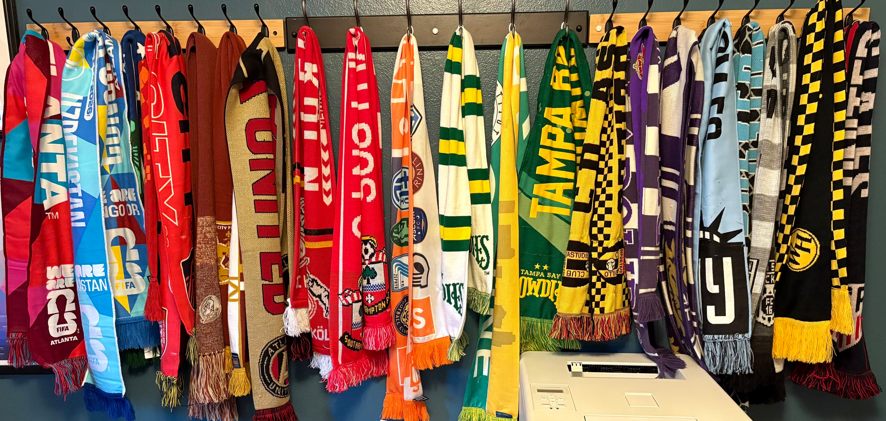 A collection of multi-colored soccer scarves hanging on a blue wall