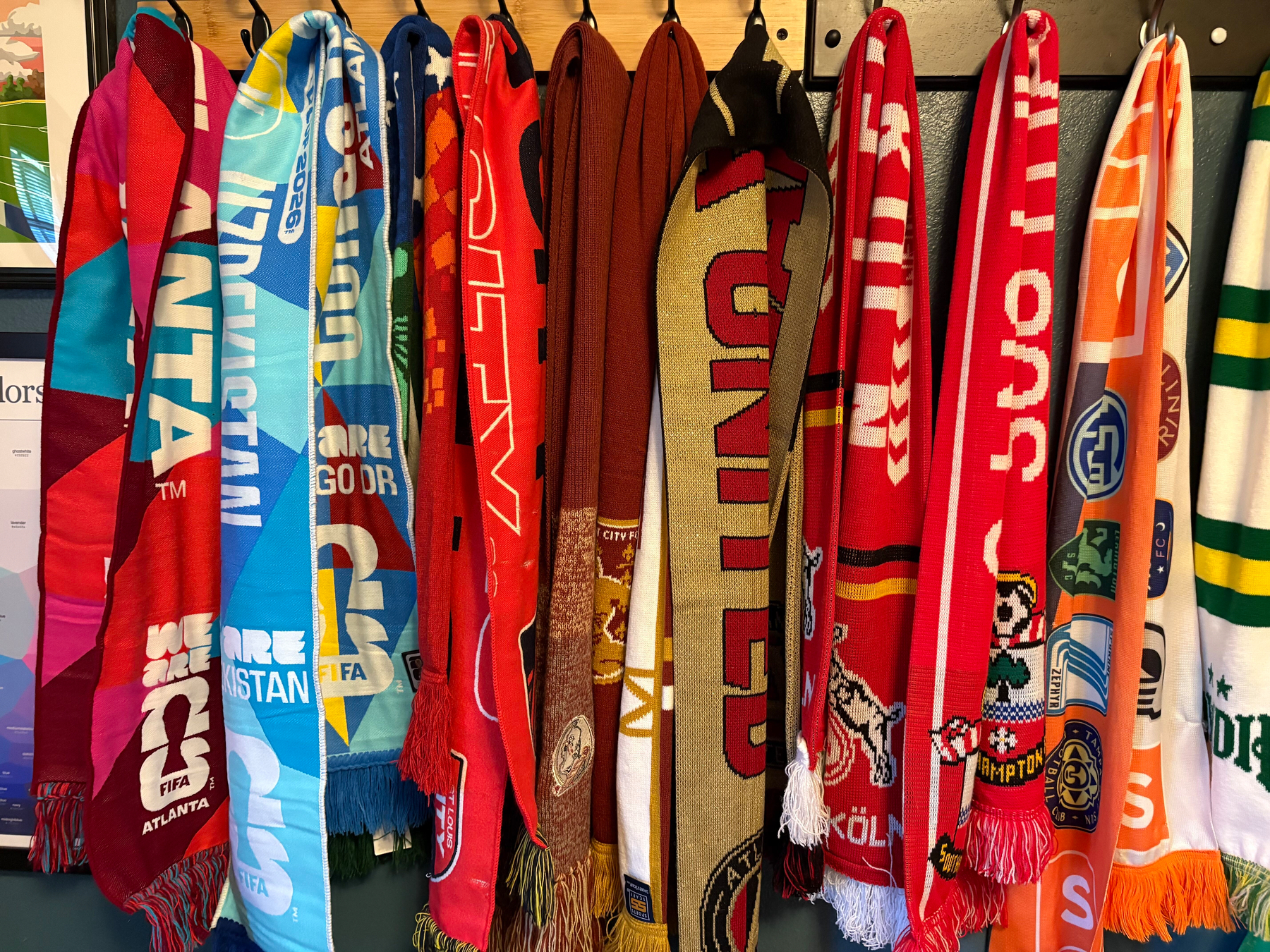 A collection of multi-colored soccer scarves hanging on a blue wall, half of the scarves shown in the previous photo