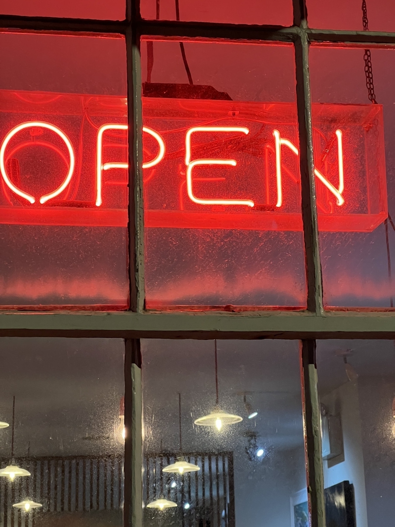 A neon "OPEN" sign is glowing brightly behind a window, casting a red hue inside.