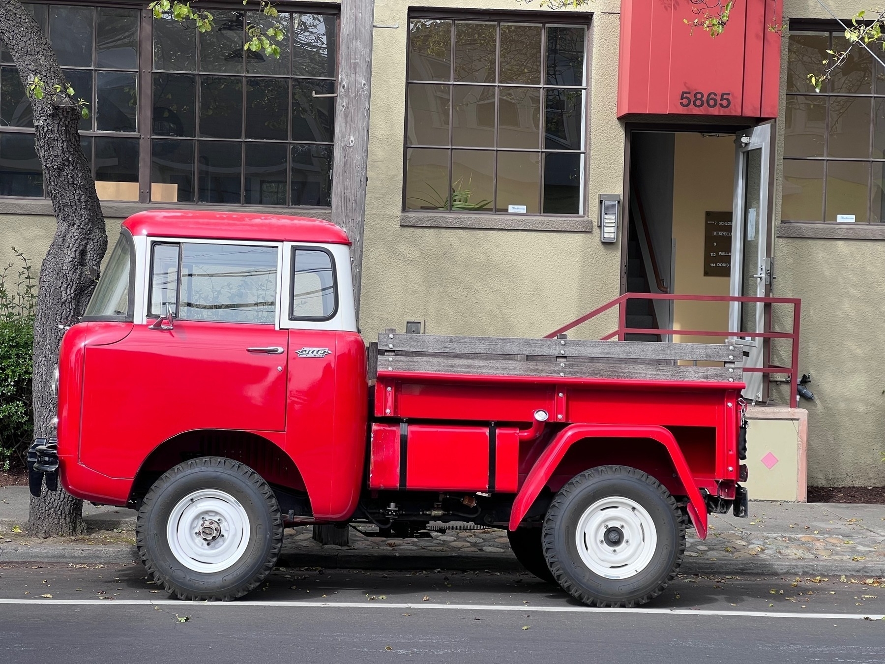 A red pickup truck -- old an of indeterminate origin -- parked on the street in front of a building