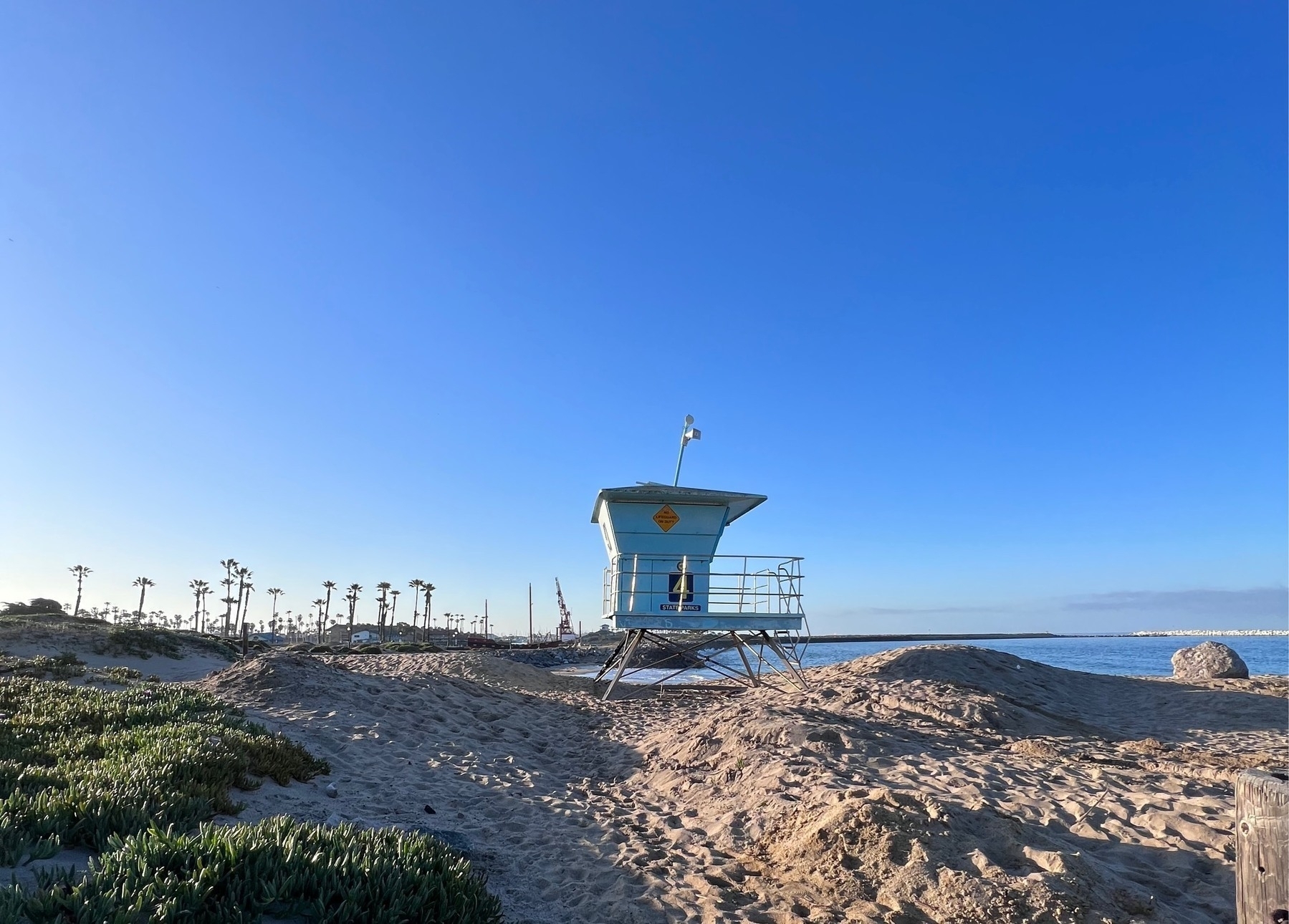 Beach with an empty teal lifeguard tower in the mid ground. 