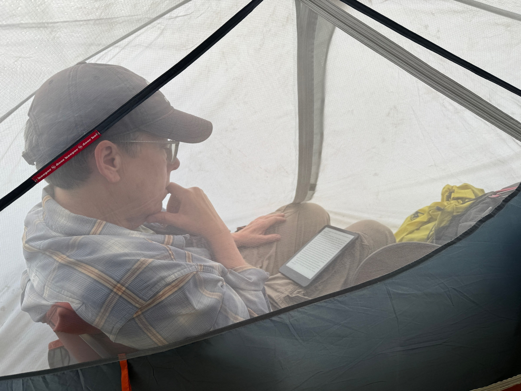 Marnie, in the tent vestibule, out of the heavy morning fog, reading. 