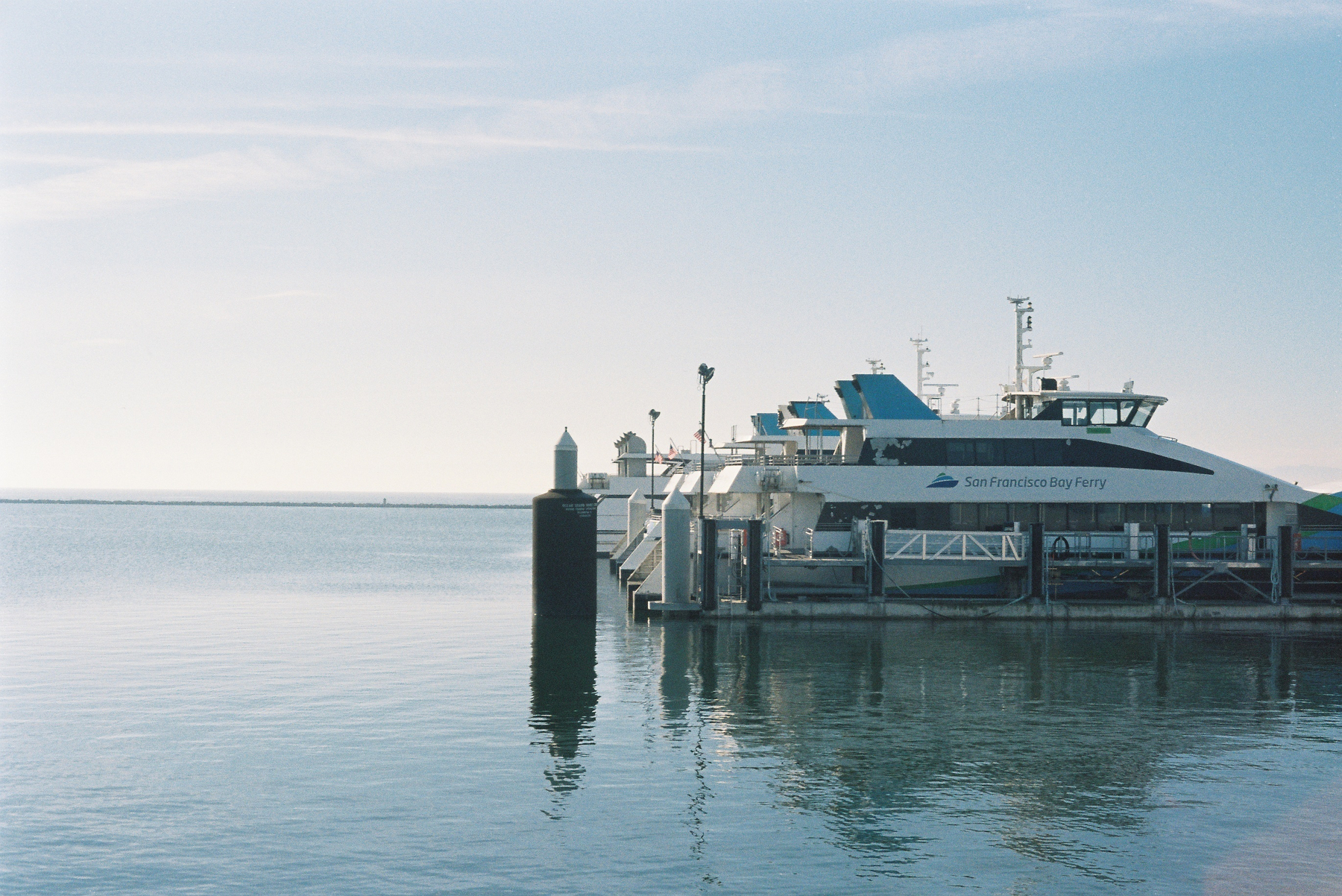 A ferry is docked at a pier on a calm body of water with a clear sky in the background.