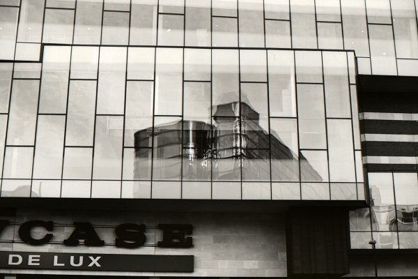 A monochrome photograph showing a partial reflection of a building in the windows of the building opposite.