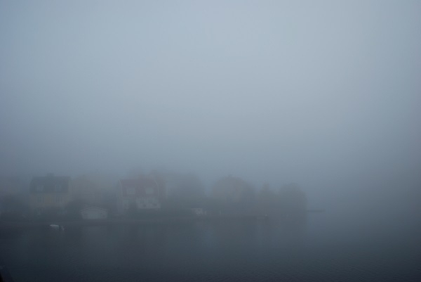 Some houses on an island barely visible in thick fog.