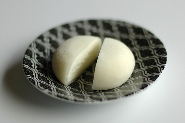 Mochi with coconut ice-cream, cut in half, on a black and white saucer.