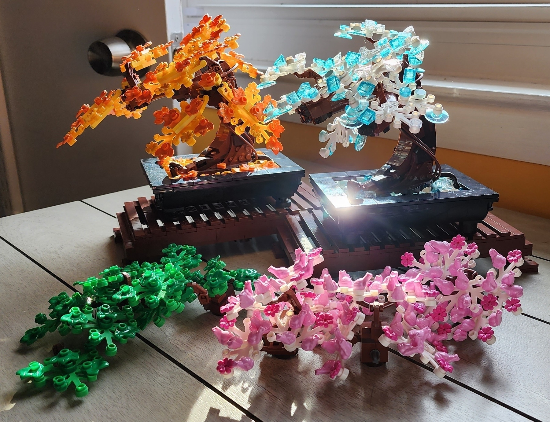 2 built Lego Bonsai sets with fall leaves and icy winter branches respectively, displayed alongside the original green branches and spring cherry blossom versions.