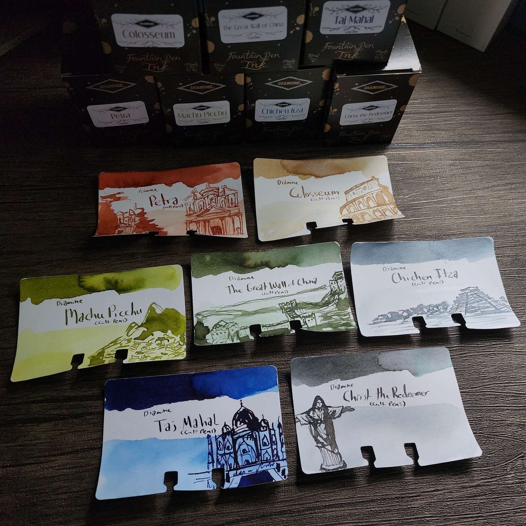 Set of 7 inks and card swatches for the Cult Pens Exclusive Diamine inks featuring Wonders of the World: Petra (a medium orange red), Colostrum (parchment brown), Machu Picchu (spring green), The Great Wall of China (dark green), Chichen Itza (light blue/gray), Taj Mahal (vibrant dark blue) and Christ the Redeemer (medium cool grey).