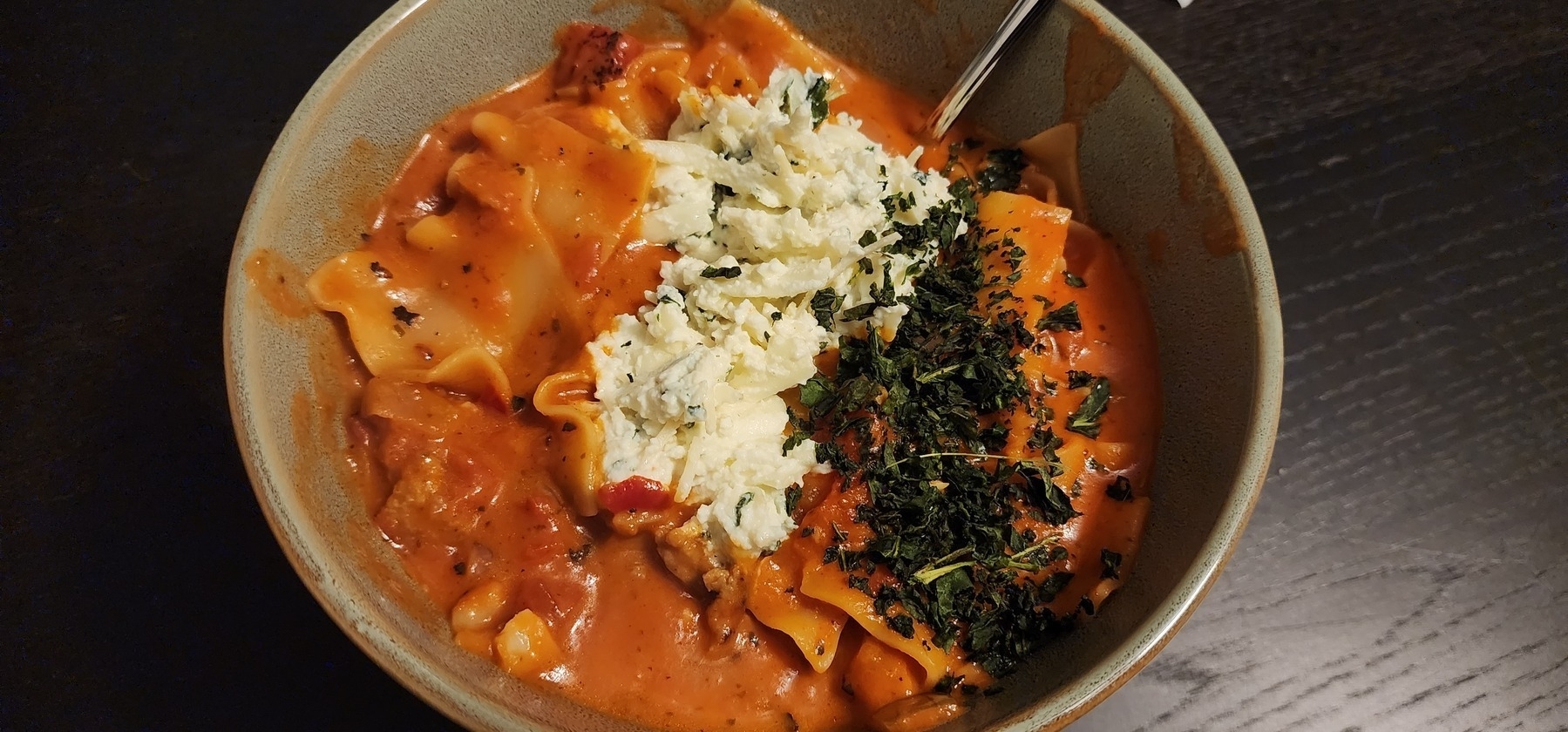 Bowl of lasagna soup with small lasagna noodles in a tomato cream sauce topped with ricotta, mozzarella, parmasean, and basil