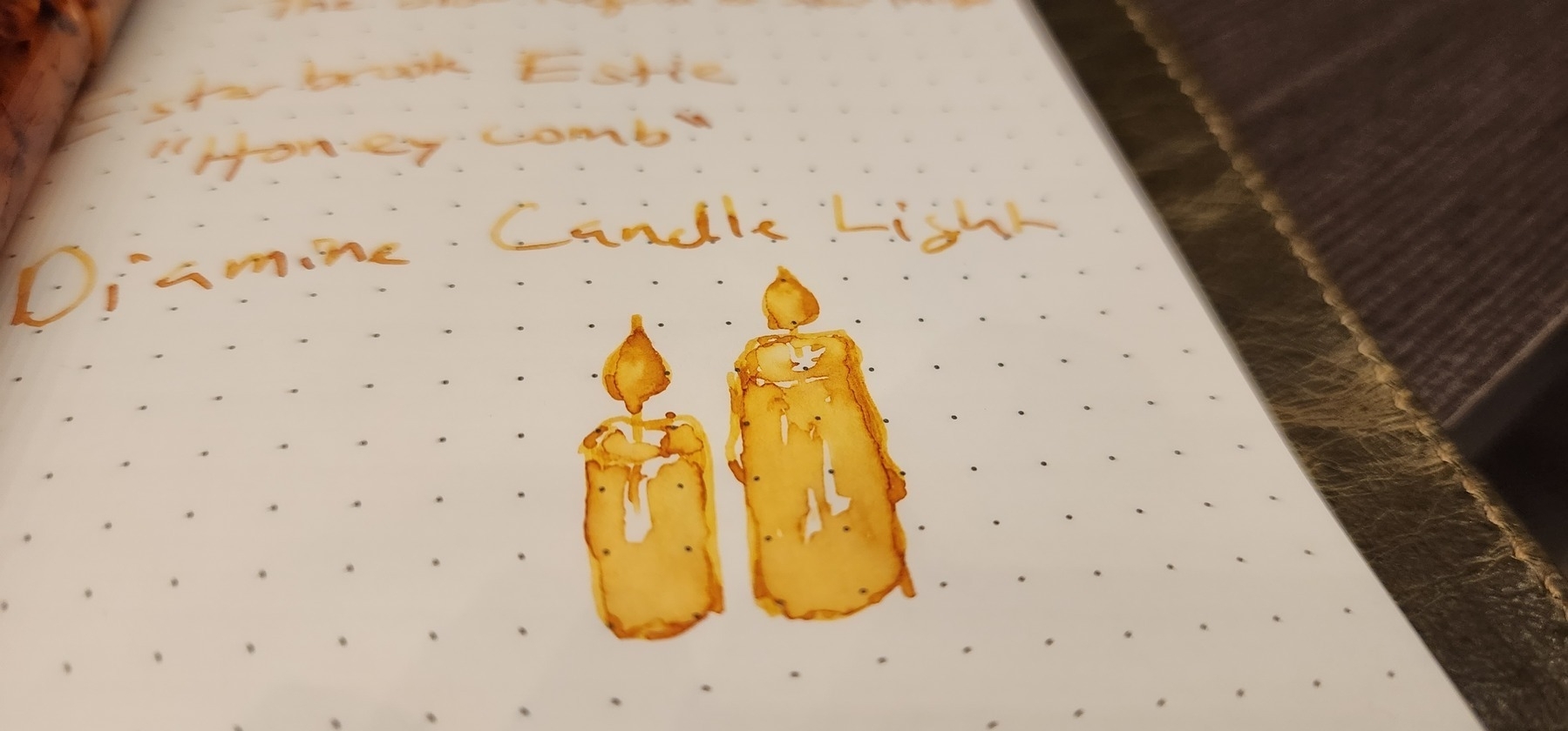 Photo of dot-grid notebook with writing in yellow Diamine Candle Light ink including rough sketch of two lit candles.