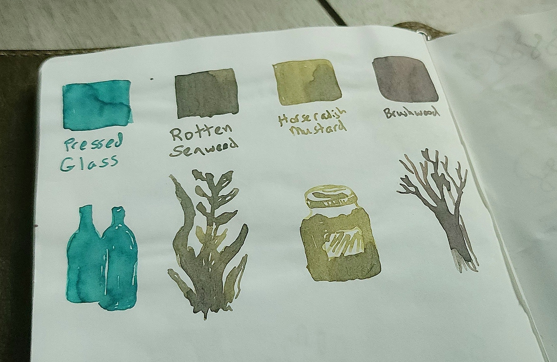 Photo of notebook with writing/drawing samples of four ink colors: pressed glass, rotten seaweed, horseradish mustard, brushwood