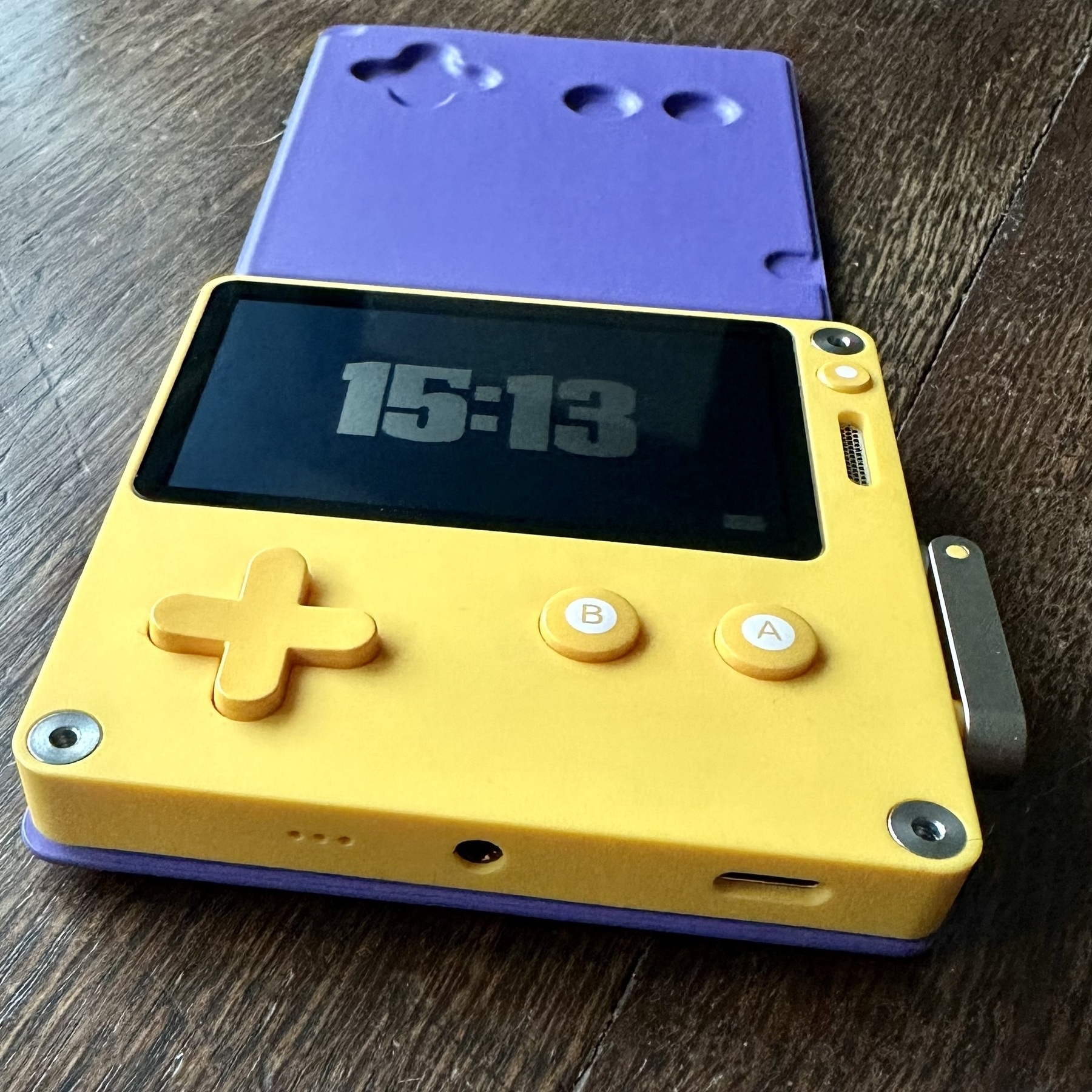 Playdate handheld game system, in standby mode with open purple cover