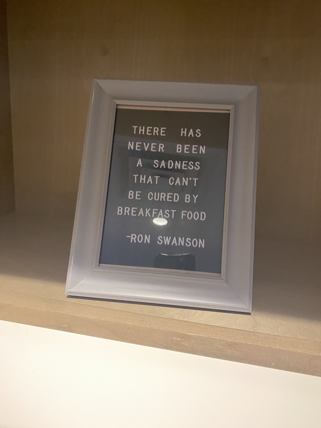 Poorly lit picture frame with quote from fictional character Ron Swanson. It reads “There has never been a sadness that can’t be cured by breakfast food.”