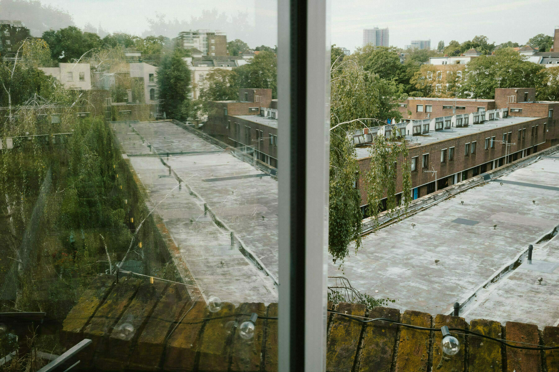 View from a high balcony looking out over low council terraces and trees. A bar runs through the centre of the frame and the left hand side of the frame is a misaligned reflection of the view on the right 