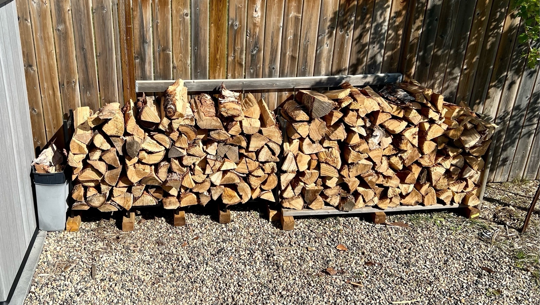 a ohoto of a bunch of wood chopped for firewood agaiinst a fence. 