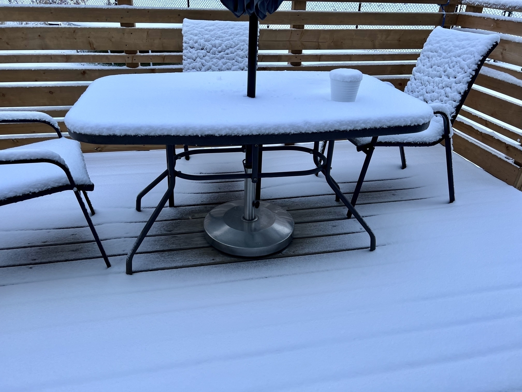Deck with table and 2 chairs all with a covering of an inch or two of snow. 