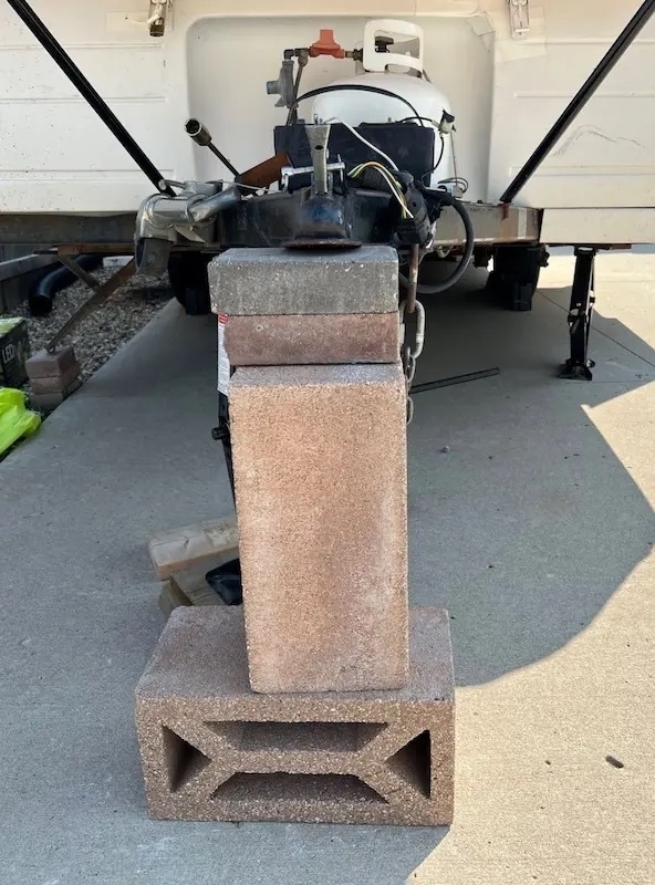 A photo of a tent trailer hitch being supported by cement blocks and patio stones in an unstable manner to represent my current blogging platform.