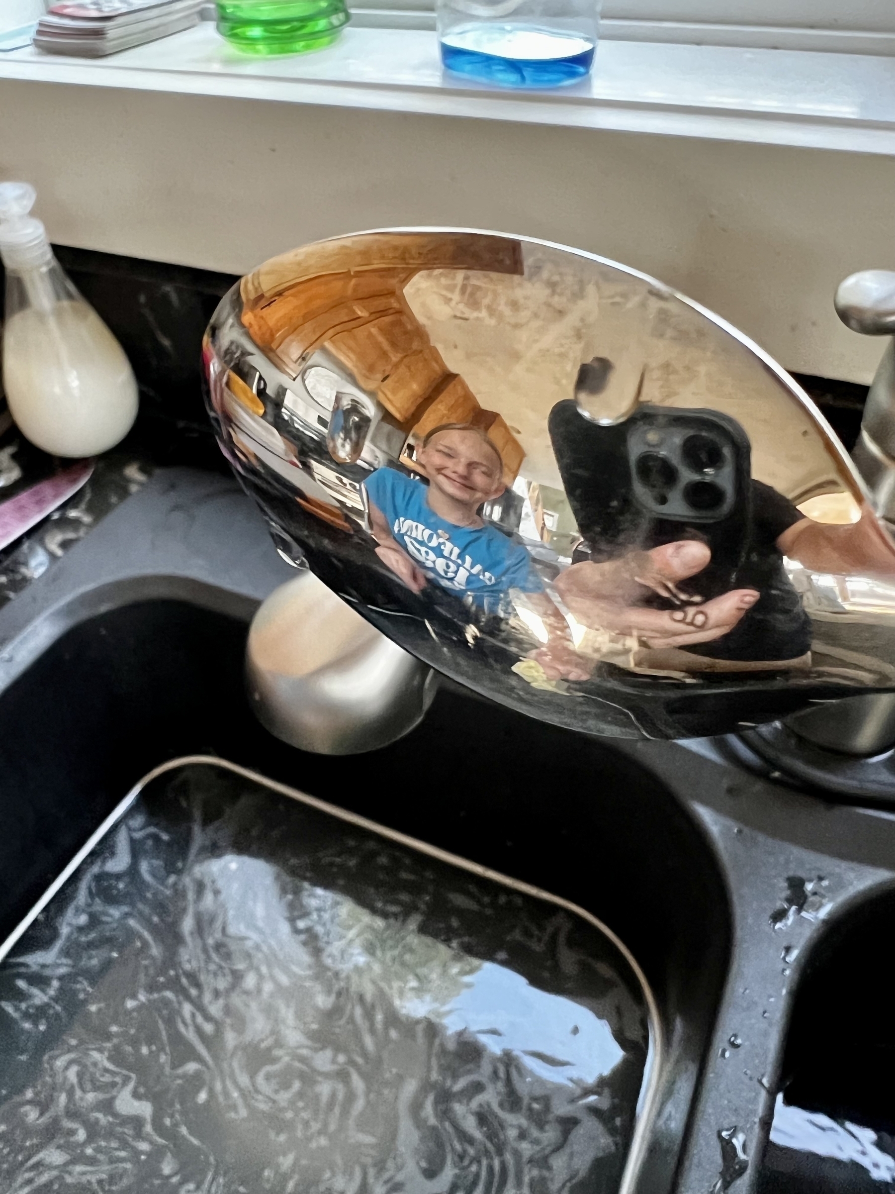 Picture of a sink with a spoon held so you can see a kid’s vague reflection in the spoon. 