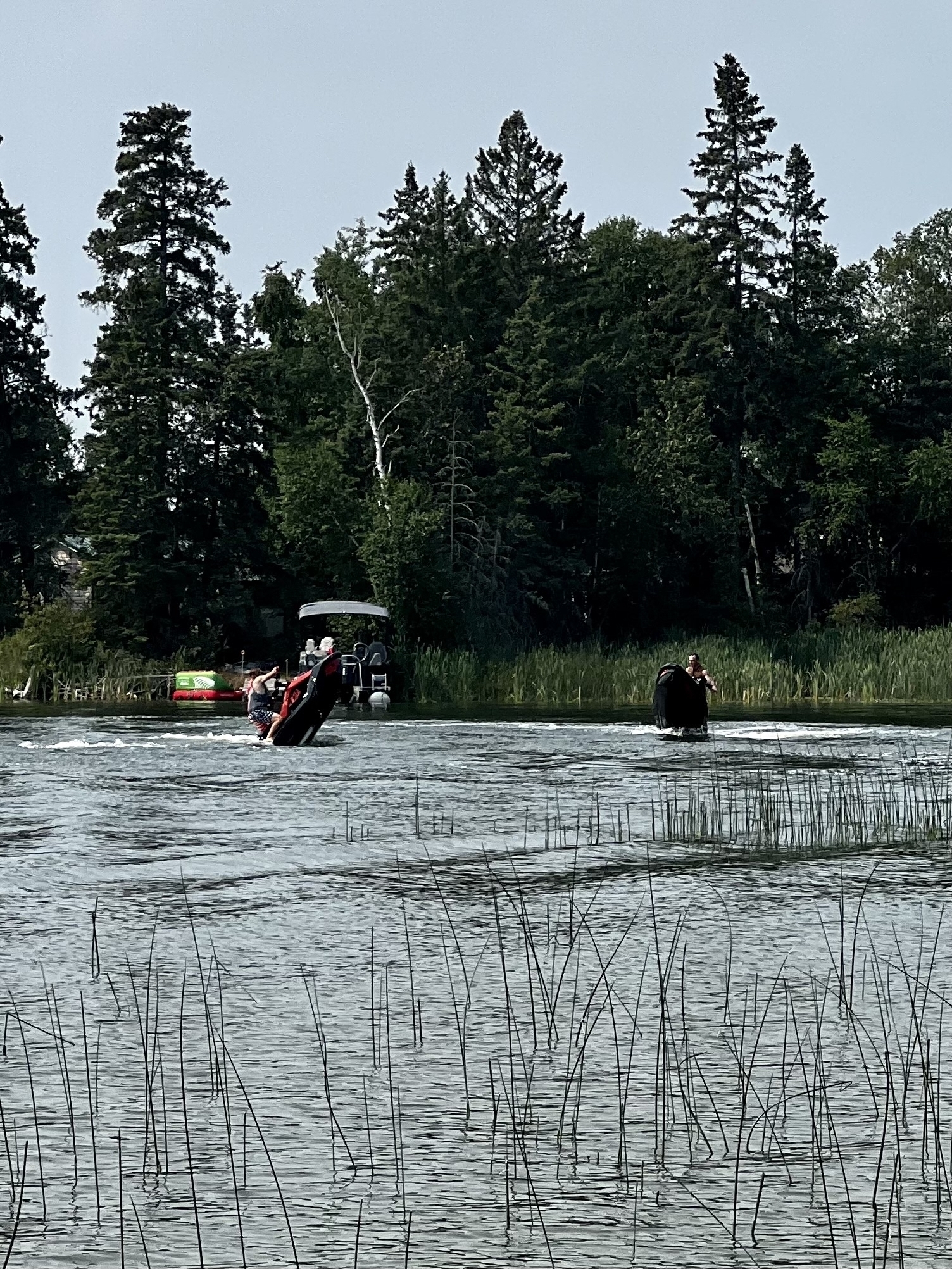 Two dudes are each driving some form of jetski in shallow water 