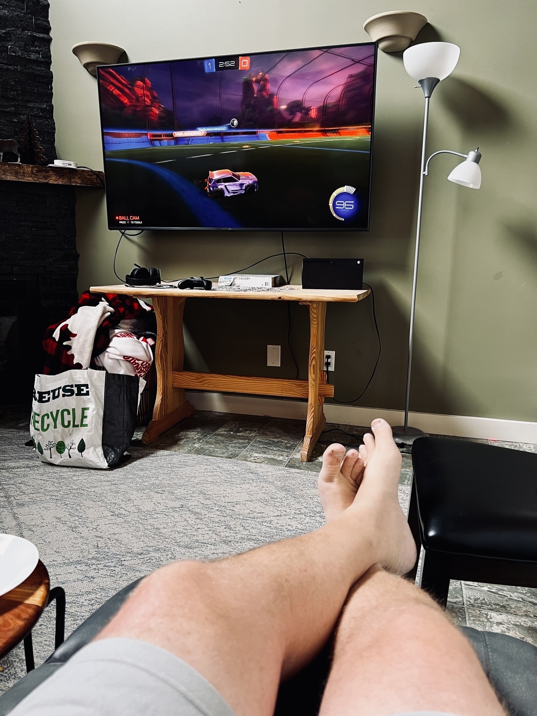 Photo of me sitting on a couch with feet up and a tv with Rocket League being played on an Xbox. 
