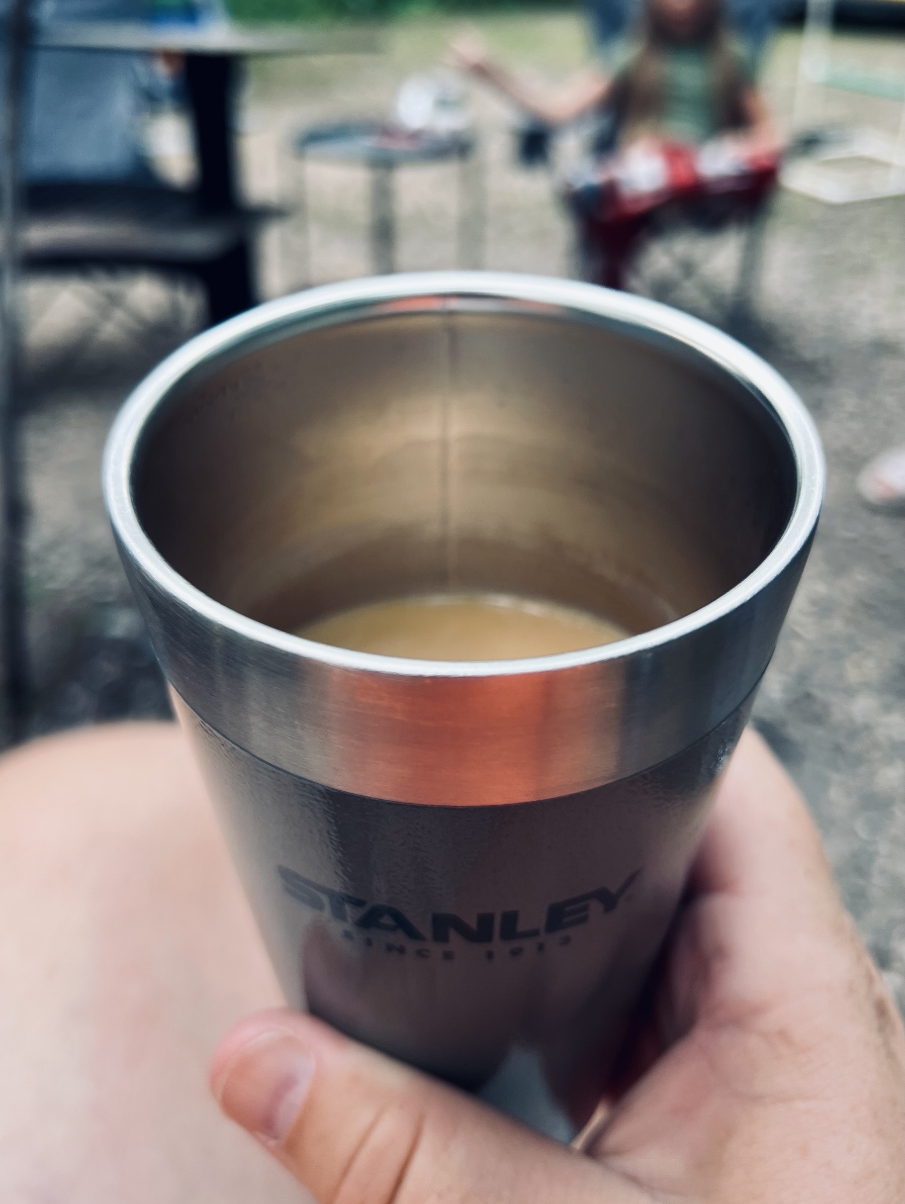 A coffee mug half filled with coffee is in a man’s hand. The coffee mug has a STANLEY branding printed on the side. 