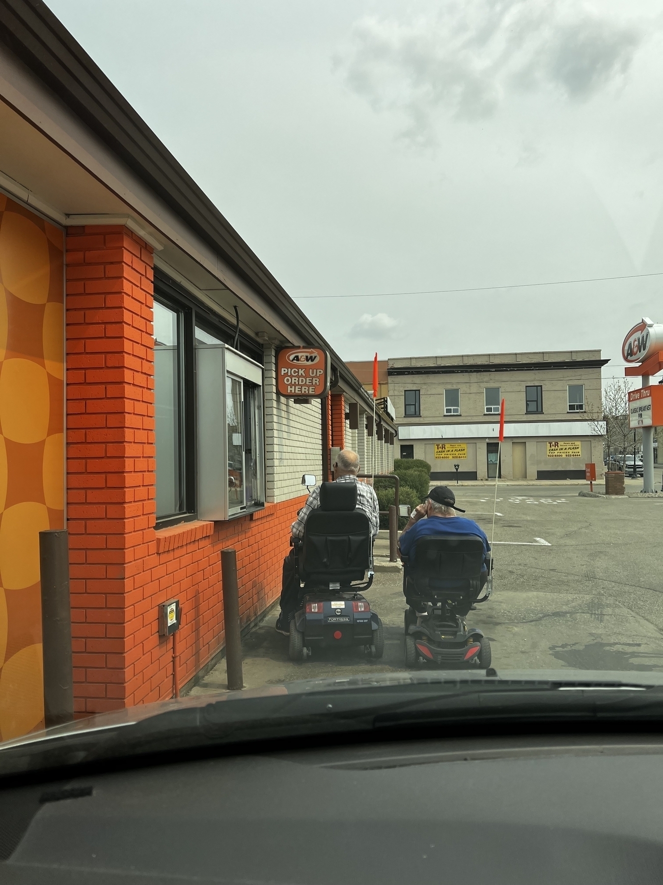 An older couple each on a scooter at a A&W drive through. 