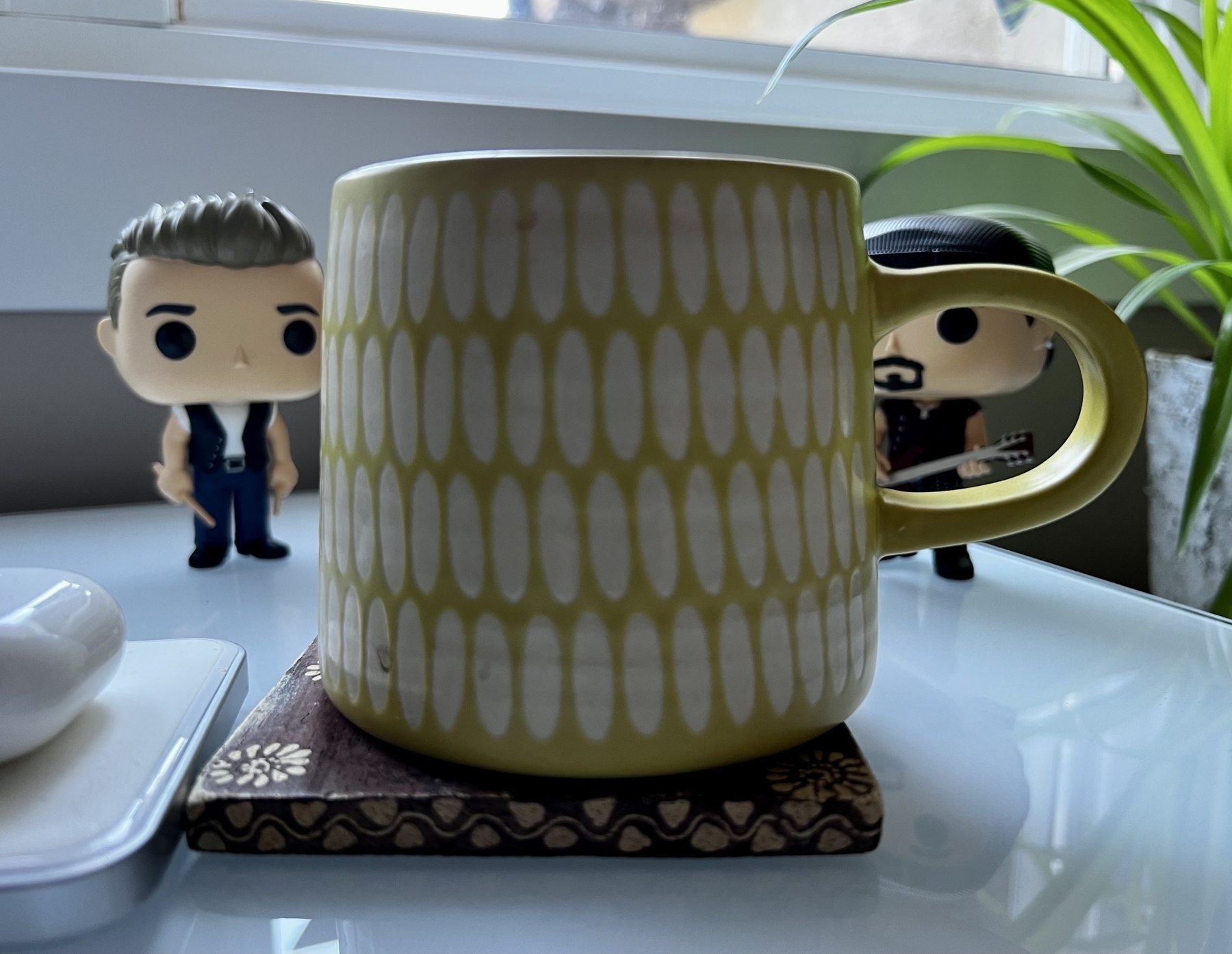 A yellow mug in the foreground with a couple of members of U2 as Funko Pop toys in the background.