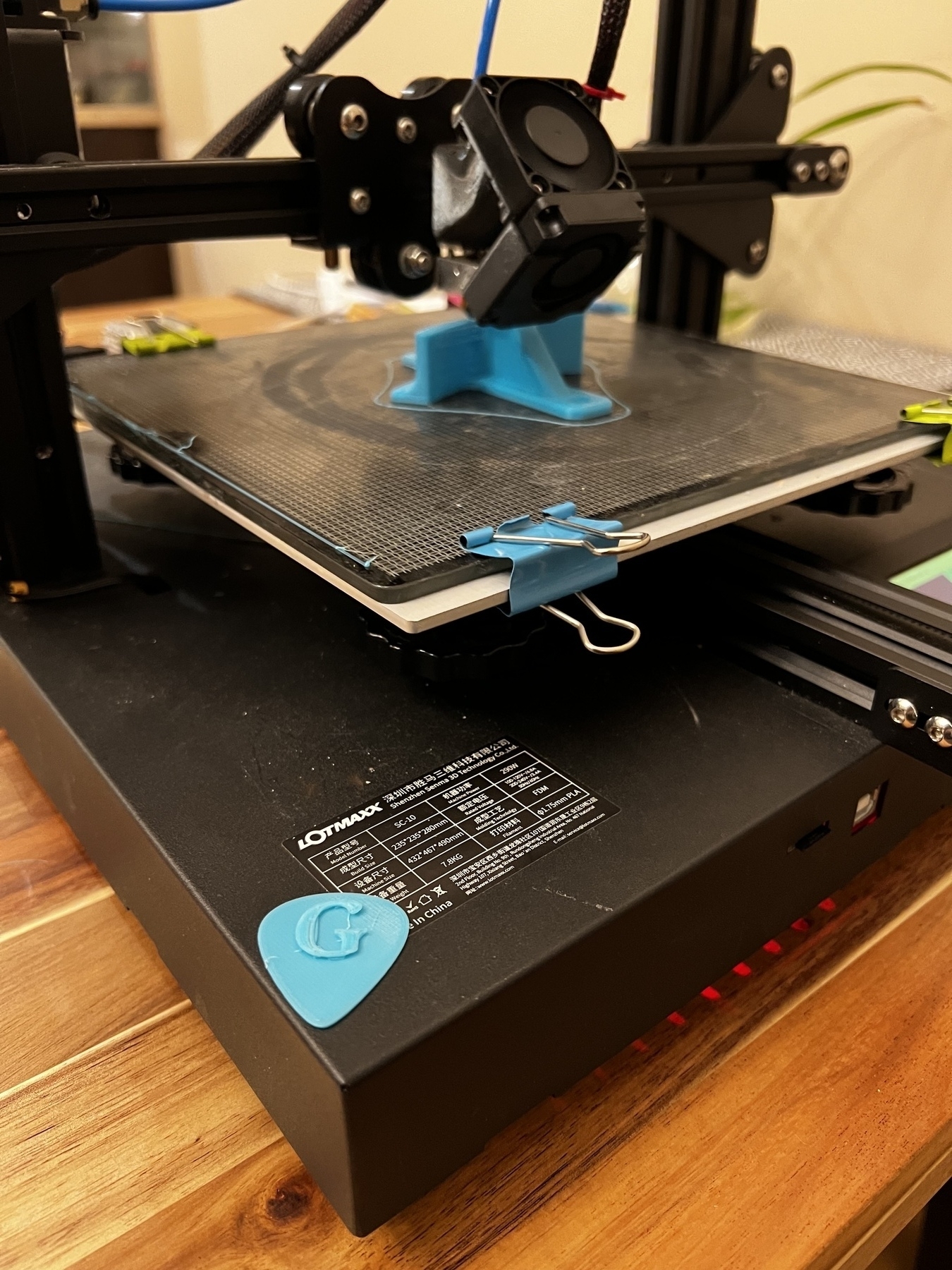 A 3D printer with a printed guitar pic on the side of it while a headphone holder is being printed. 