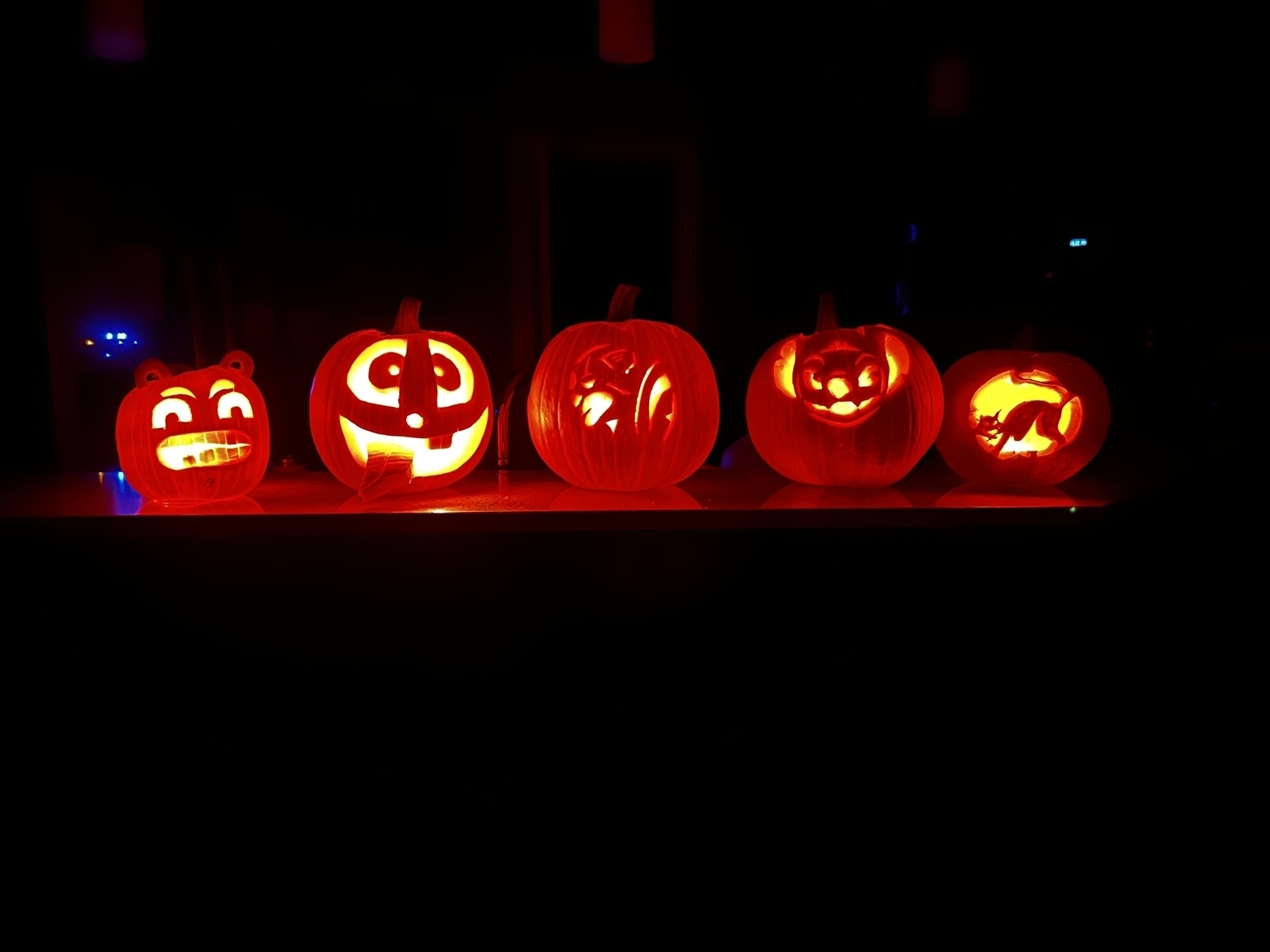 5 pumpkins in a row carved with candles lighting from the inside 