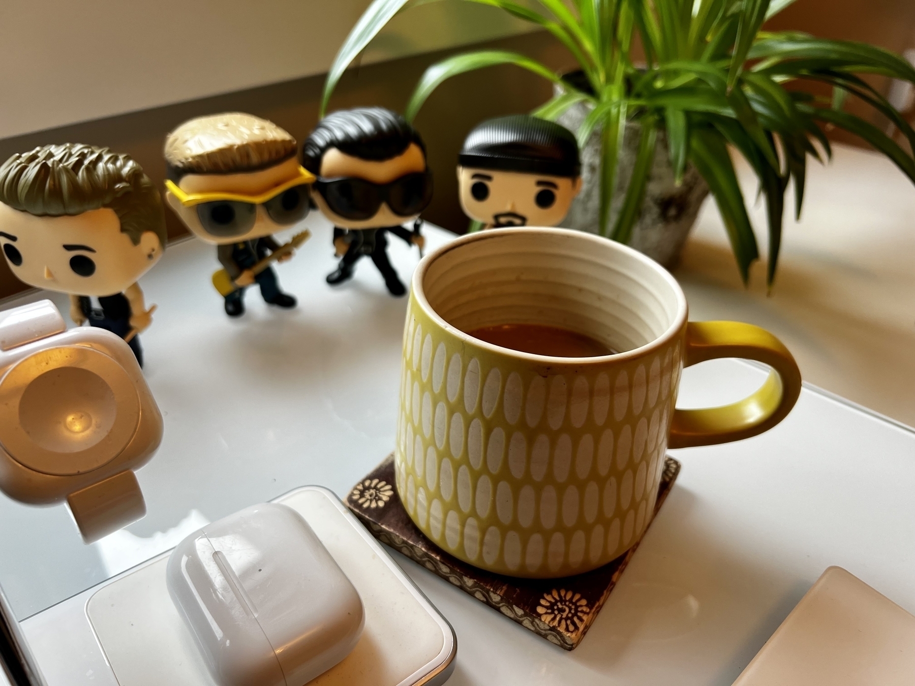 A yellow coffee mug in the foreground, with Funkopop u2 characters in the background. 