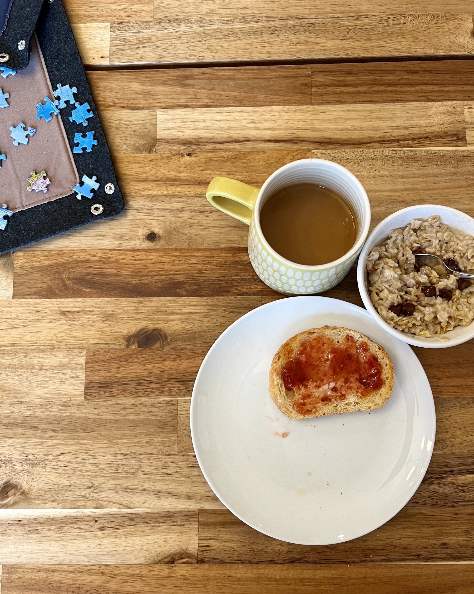 A plate with piece of toast, a bowl of oatmeal, and a cup of coffee on a table. 