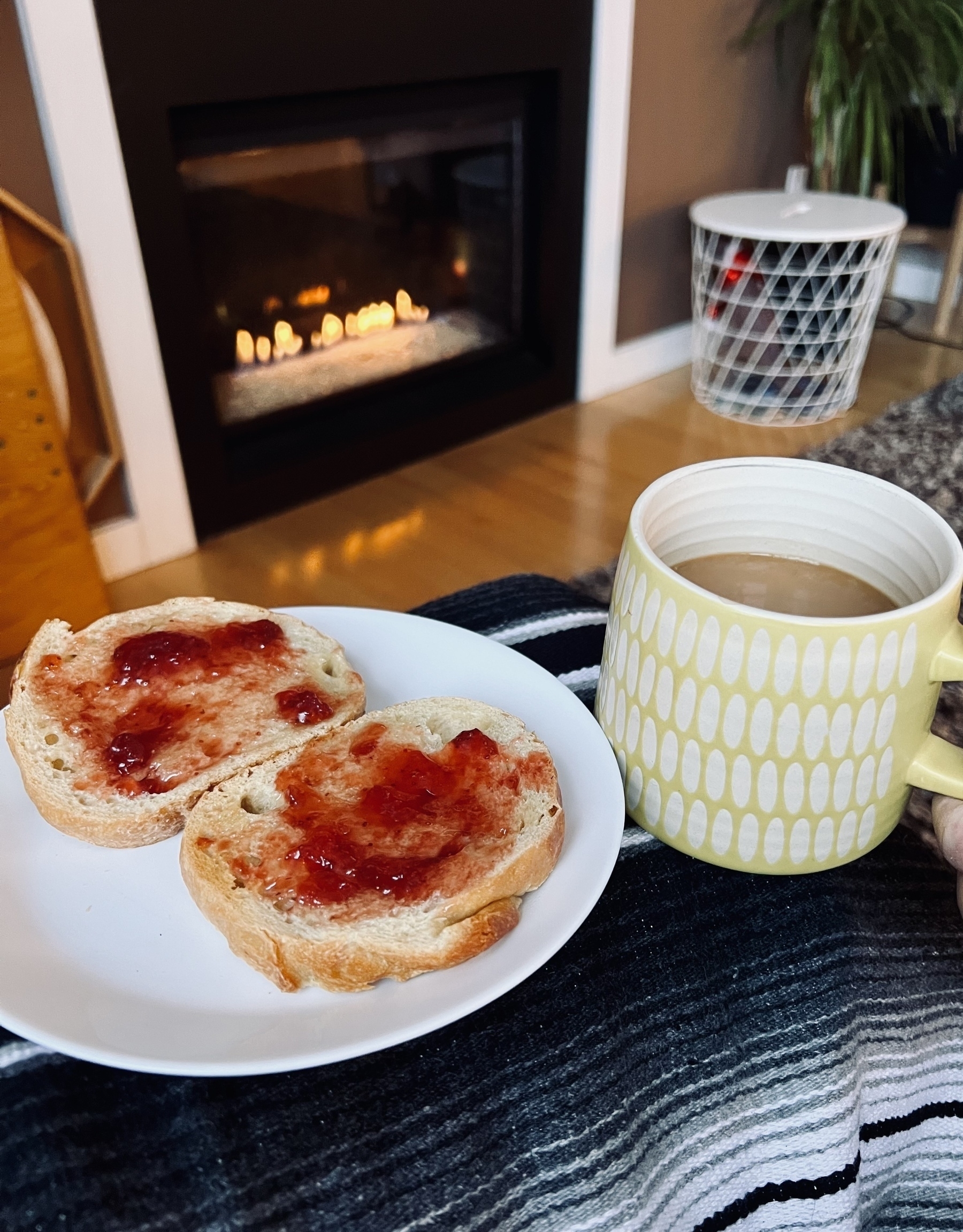 Two pieces of sourdough toasted with butter and jam, a cup of coffee, and a natural gas fire in the background. 