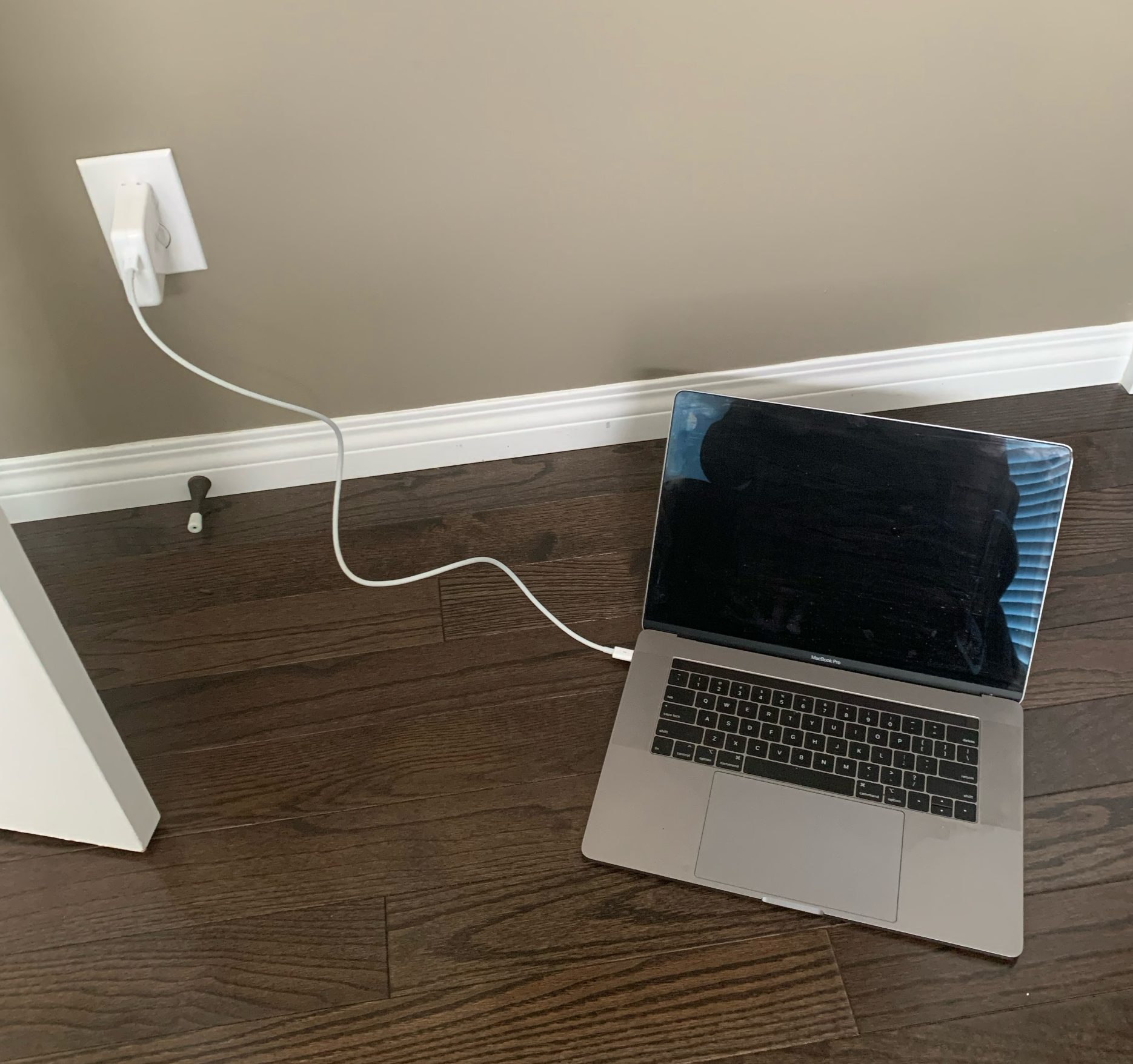 A MacBook Pro on the floor next do a door plugged into a charger with a 2ft long white cable.