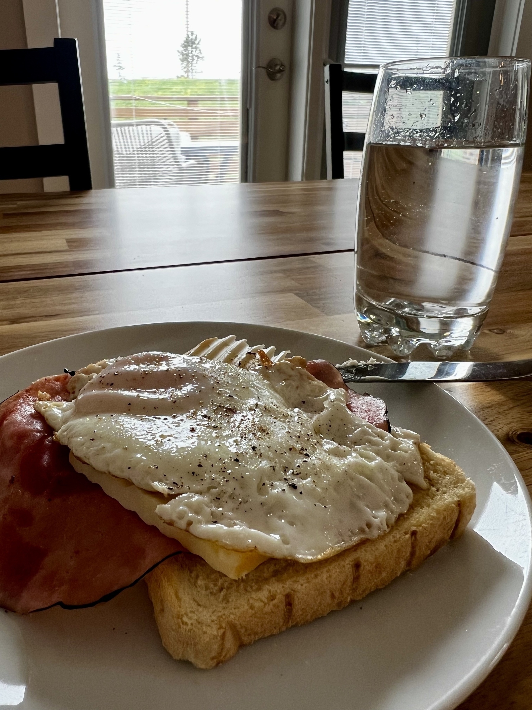 Fried egg on toast on a plate on a table. With a glass of water on the side. 
