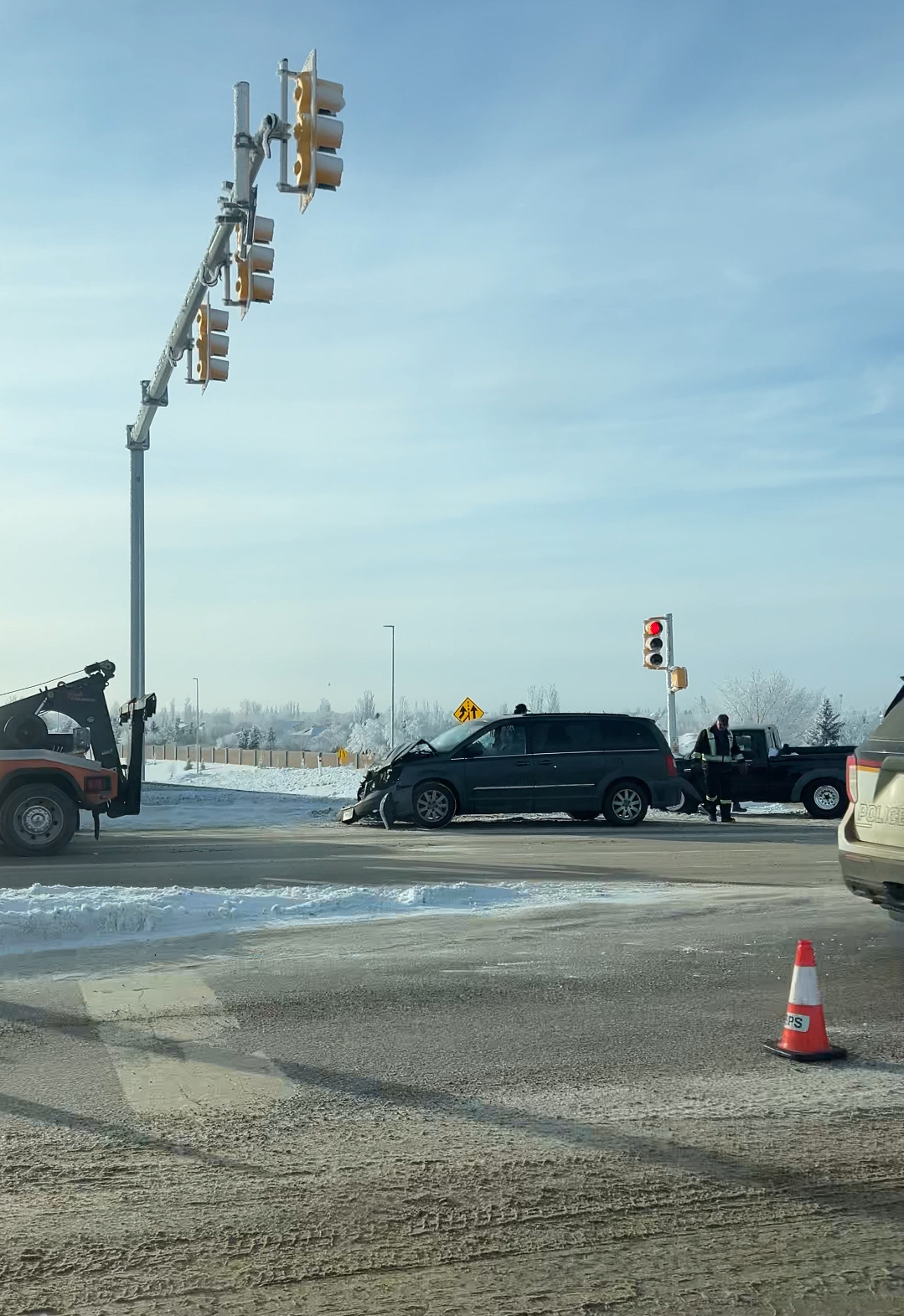 A tow truck is at an intersection assisting a black SUV with front-end damage, and a traffic cone is placed nearby.