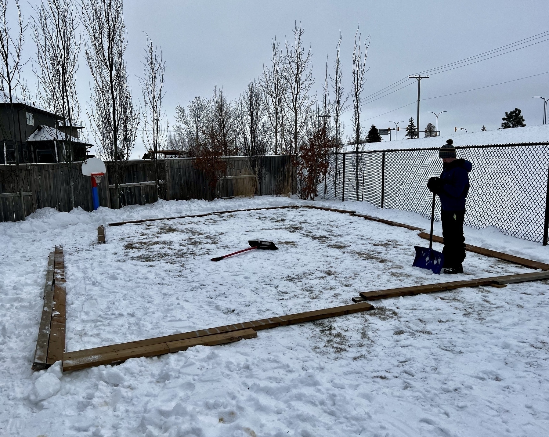 A backyard with boards laying on the ground and a kid holding a shovel. 