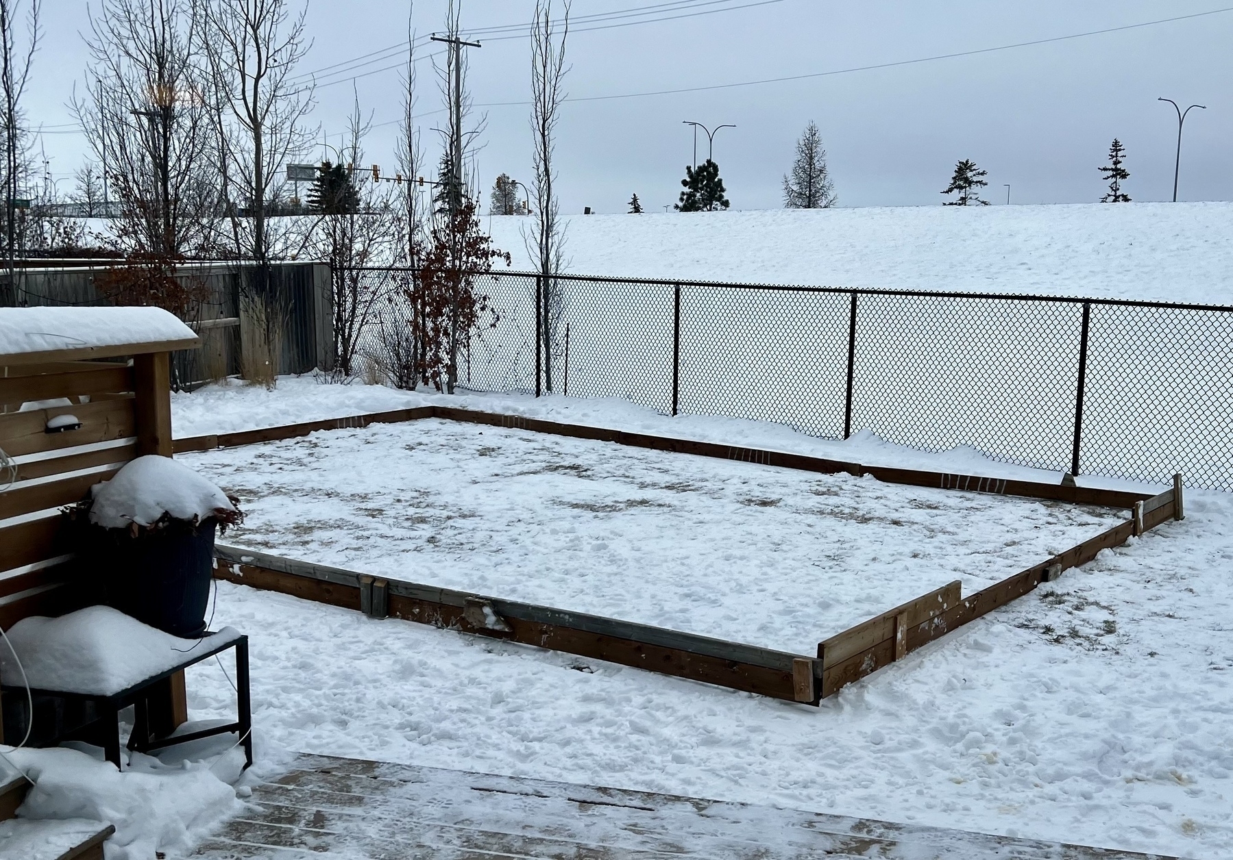 A snow-covered backyard features a large, framed rectangular area for a backyard rink or ODR as the kids say. 