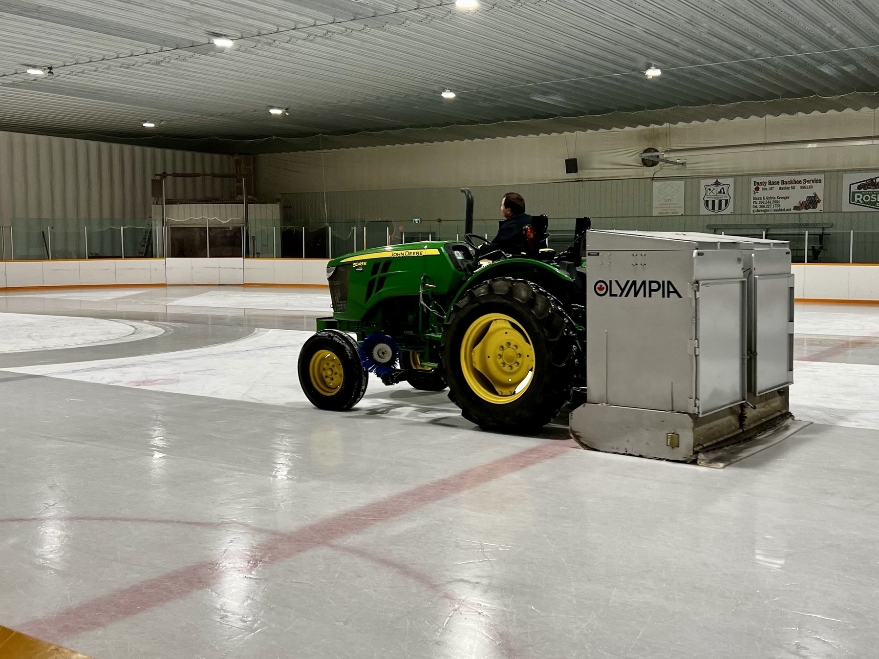 A tractor with a Zamboni ice cleaning attachment on the back clearing the ice in a rink. 